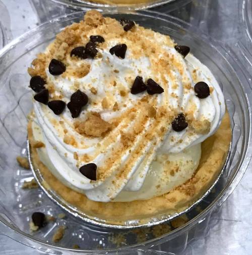 A close-up of a dessert cup with whipped cream, chocolate chips, and crumbled cookie topping.