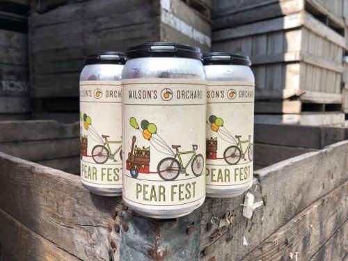 Three cans of "Pear Fest" beer with a bicycle graphic, set against a backdrop of wooden crates.
