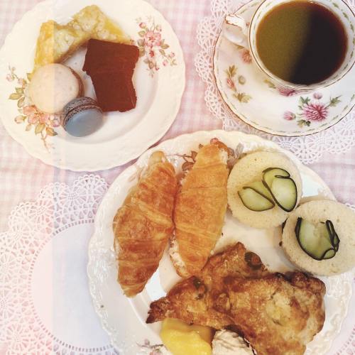 A plate of pastries, including croissants and sweets, alongside a cup of tea on a lace tablecloth.