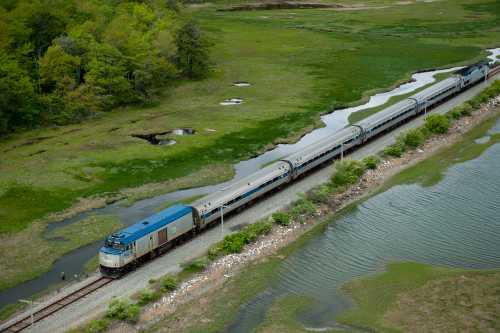 A train travels along a track beside a winding river and lush green landscape.