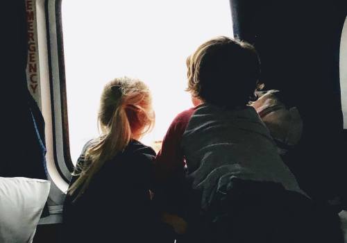 Two children looking out a window, their backs to the camera, with soft light illuminating the scene.