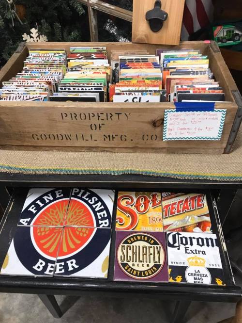 A wooden crate filled with vintage beer labels and postcards, labeled "Property of Goodwill MFG Co." on a table.