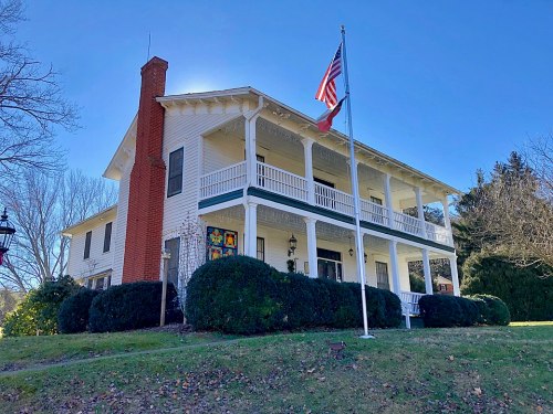 A two-story white house with a porch, American flag, and landscaped yard on a clear day.