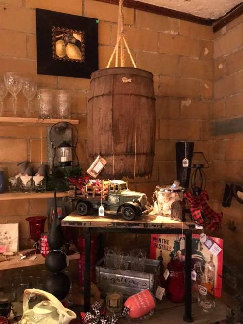 A rustic display featuring a hanging barrel, vintage truck, and various decorative items on a wooden table.