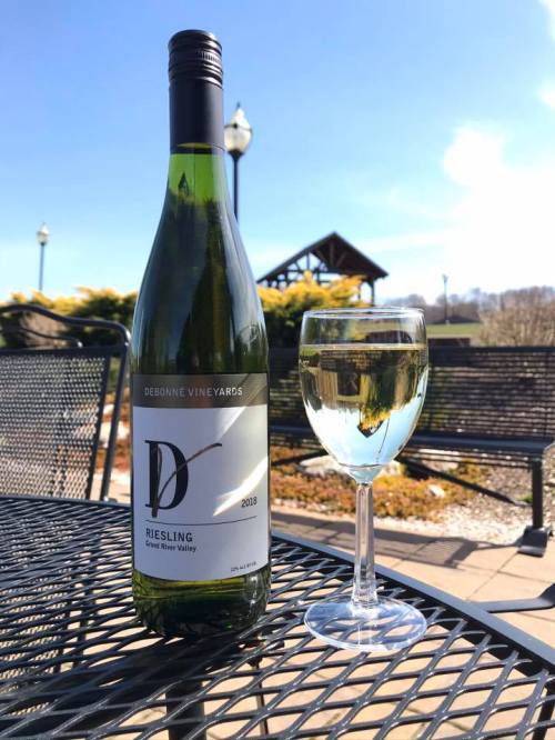 A bottle of Riesling wine next to a glass of wine on a table outdoors, with a clear blue sky in the background.