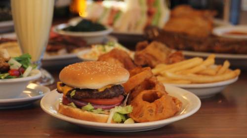 A plate featuring a cheeseburger with lettuce, tomato, onion, onion rings, and fries, with other dishes in the background.