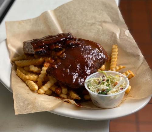 A plate of BBQ ribs with sauce, served with crinkle-cut fries and a side of coleslaw in a small cup.