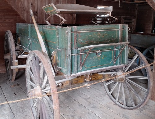 A vintage wooden cart with green paint and metal accents, resting on wooden flooring in a rustic setting.
