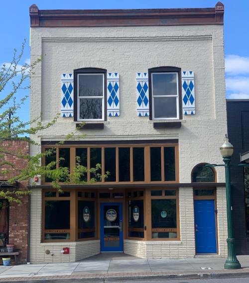 A two-story building with blue and white diamond-patterned shutters and large windows, featuring a blue door.
