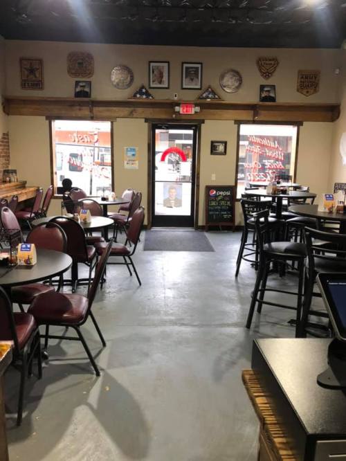 Interior of a casual dining restaurant with empty tables, a counter, and a door leading outside. Decorated with wall art.