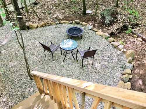 A cozy outdoor seating area with two chairs and a table, surrounded by gravel and trees in a wooded setting.