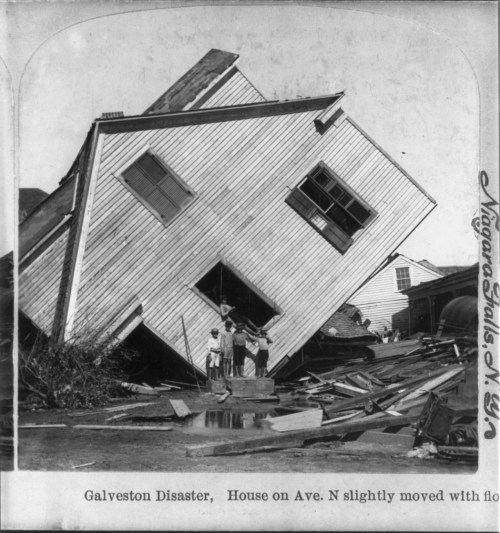 A tilted house with four people standing nearby, surrounded by debris from the Galveston disaster.