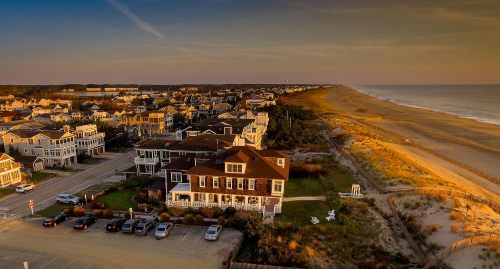 Aerial view of a coastal town at sunset, featuring beach houses and a sandy shoreline.