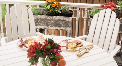 A cozy outdoor dining setup with two plates of food on a white table, surrounded by flowers in pots.