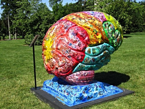 Colorful brain sculpture with intricate designs, set on a grassy area surrounded by trees.