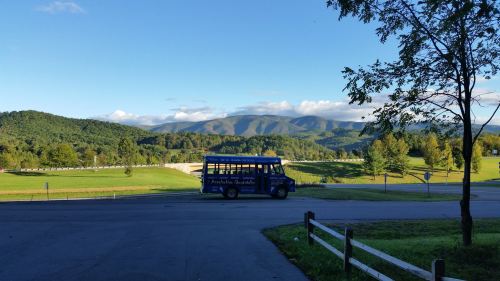 A blue bus parked near a scenic view of rolling hills and mountains under a clear blue sky.