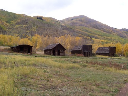 A row of rustic wooden cabins surrounded by colorful autumn trees and rolling hills.
