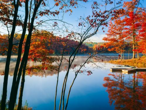 A serene lake surrounded by vibrant autumn trees reflecting in the water under a clear blue sky.