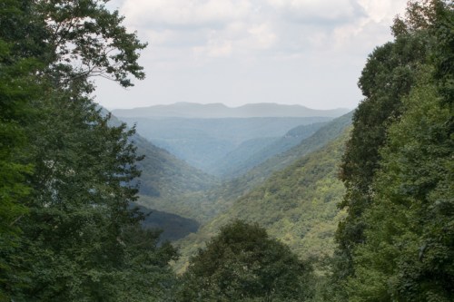 A scenic view of a lush green valley surrounded by mountains under a cloudy sky.