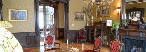Elegant vintage room with ornate furniture, rich wallpaper, and decorative art, featuring a chandelier and a fireplace.