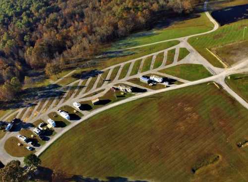 Aerial view of a campground with several RVs parked on grassy sites surrounded by trees and open fields.