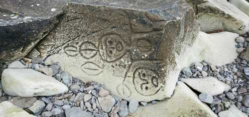 Ancient rock carvings on a stone surface, surrounded by small pebbles and larger rocks.