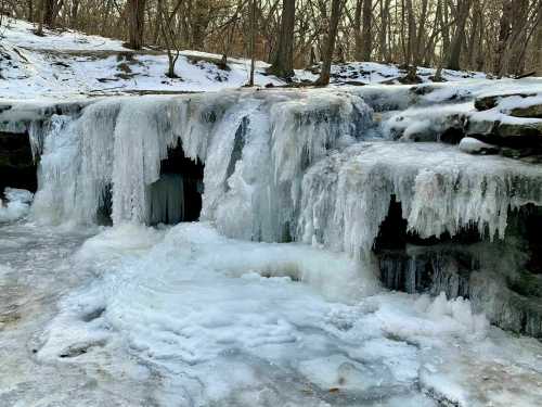 A frozen waterfall surrounded by snow-covered rocks and trees in a winter landscape.