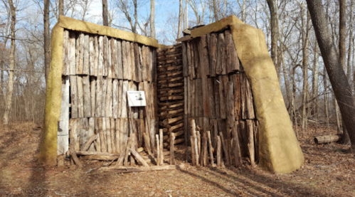 A rustic wooden structure with a sloped roof, surrounded by trees in a forested area.