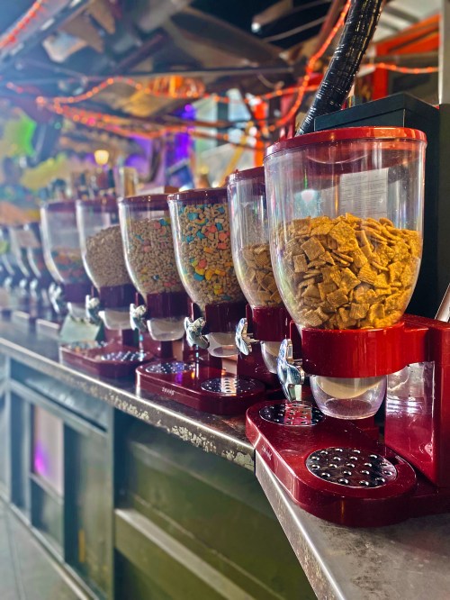 A row of colorful cereal dispensers on a bar counter, filled with various types of cereal.