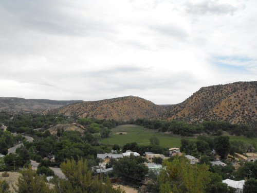 A scenic view of rolling hills and a small town surrounded by greenery under a cloudy sky.