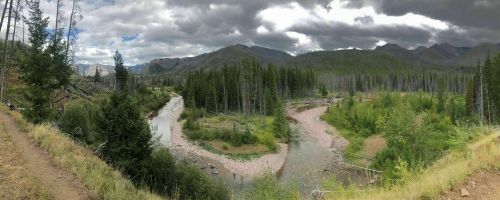A panoramic view of a winding river surrounded by lush greenery and mountains under a cloudy sky.