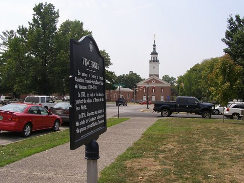 Historical marker in foreground with a church and trees in the background, showcasing a scenic town square.