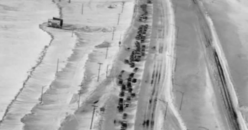 Aerial view of a snow-covered road with a long line of vehicles stuck in snowdrifts.