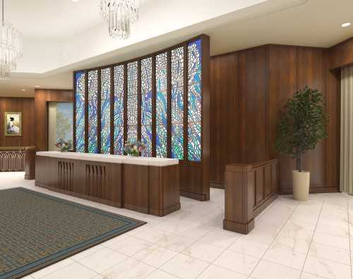 Elegant lobby with a wooden reception desk, stained glass wall, and decorative plants, featuring a plush area rug.