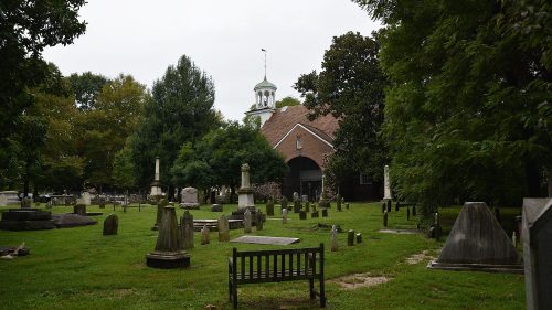 A peaceful cemetery with various gravestones, surrounded by trees and a historic building in the background.