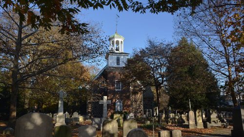 Historic church surrounded by autumn trees and a graveyard, with a clear blue sky in the background.