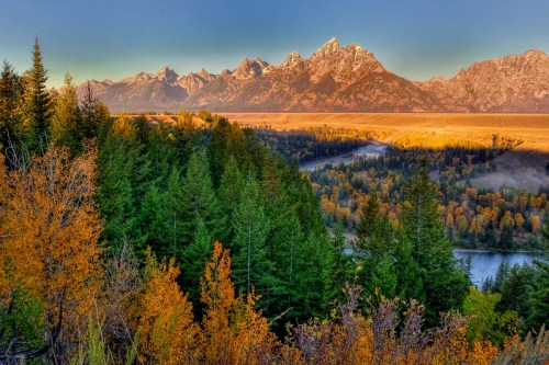A scenic view of mountains and a river surrounded by vibrant autumn foliage and evergreen trees.