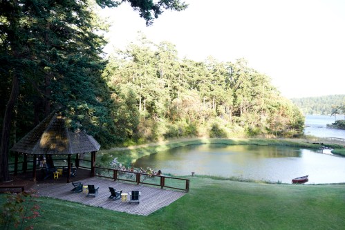 A serene lakeside scene featuring a gazebo, wooden deck, and lush greenery surrounding a calm pond.