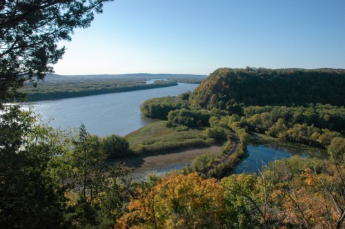 A scenic view of a winding river surrounded by lush greenery and rolling hills under a clear blue sky.