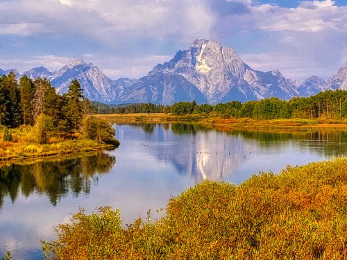 Scenic view of mountains reflecting in a calm lake, surrounded by autumn foliage and clear blue skies.