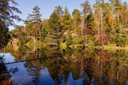 A serene lake surrounded by trees, reflecting autumn colors and a clear blue sky.
