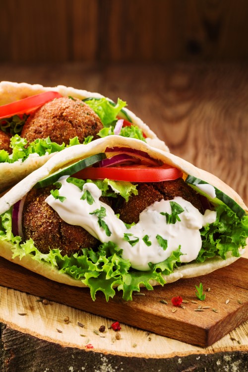 Two falafel wraps filled with lettuce, tomatoes, onions, and drizzled with sauce, served on a wooden board.