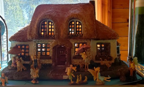 A whimsical fairy house with a thatched roof, surrounded by small fairy figurines and colorful windows.