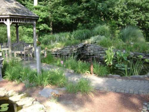 A serene garden scene featuring a pond, stone path, lush greenery, and a gazebo in the background.