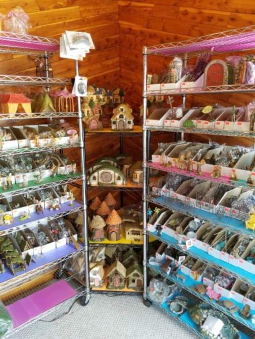 A display of various decorative miniature houses and figurines on metal shelves in a wooden room.