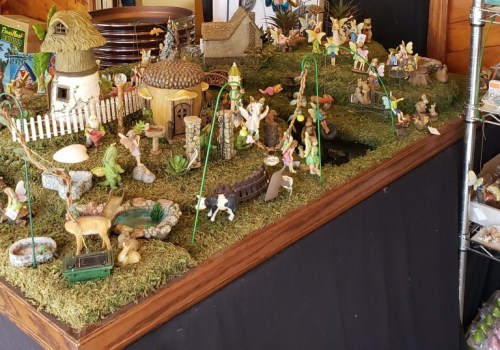 A colorful miniature village scene with figurines, greenery, and small structures on a grassy display.