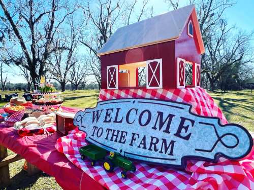 A red barn model with a "Welcome to the Farm" sign on a picnic table, surrounded by trees and a sunny outdoor setting.