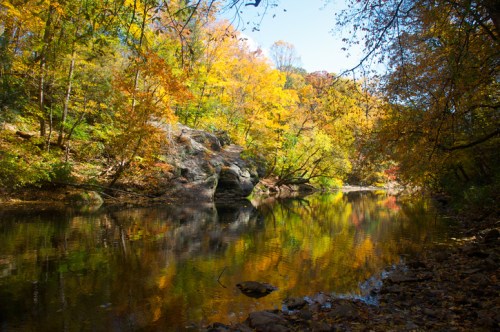 A serene river surrounded by vibrant autumn foliage and rocky banks, reflecting colorful trees in the water.