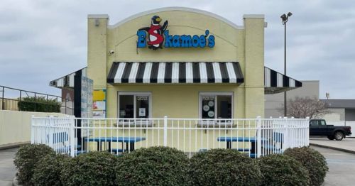A yellow building with a black and white striped awning, featuring a sign that reads "Eskamo's" and outdoor seating.