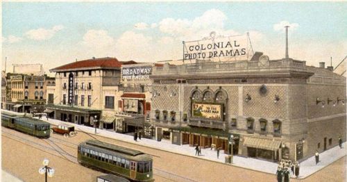 Historic street scene featuring the Colonial Photo Dramas theater and vintage streetcars.